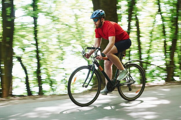 Poranna jazda. Rowerzysta na rowerze jest na asfaltowej drodze w lesie w słoneczny dzień