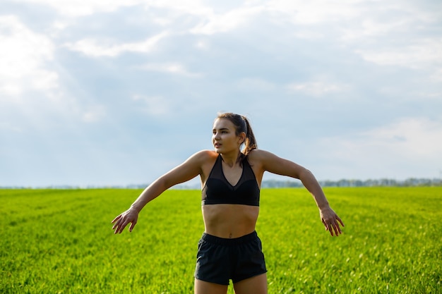 Poranny trening. Pojęcie zdrowego stylu życia. Młoda atrakcyjna kobieta w sportowej sprawia, że rozciąganie ręki przed treningiem na łonie natury o świcie. Rozgrzewanie mięśni