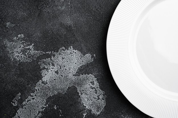 Porcelanowy pusty biały talerz z kopią miejsca na tekst lub jedzenie z kopią miejsca na tekst lub jedzenie, widok z góry płasko leżący, na tle czarnego ciemnego kamiennego stołu