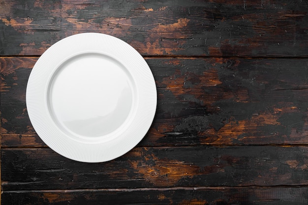 Zdjęcie porcelanowy pusty biały talerz z kopią miejsca na tekst lub jedzenie z kopią miejsca na tekst lub jedzenie, widok z góry płasko leżał, na starym ciemnym drewnianym stole tło