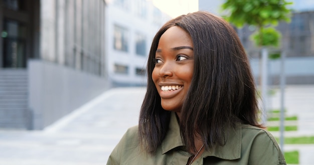 Portret African American młoda ładna kobieta stojąca na ulicy miasta i uśmiecha się radośnie do kamery.