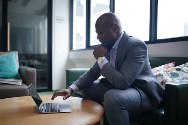 Portret afroamerykańskiego biznesmena korzystającego z laptopa lub urządzenia mobilnego w nowoczesnym biurze