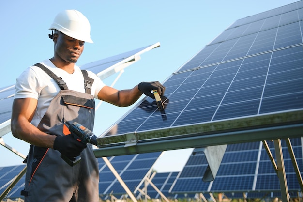 Portret afroamerykańskiego inżyniera elektryka w kasku ochronnym i mundurze instalującym panele słoneczne