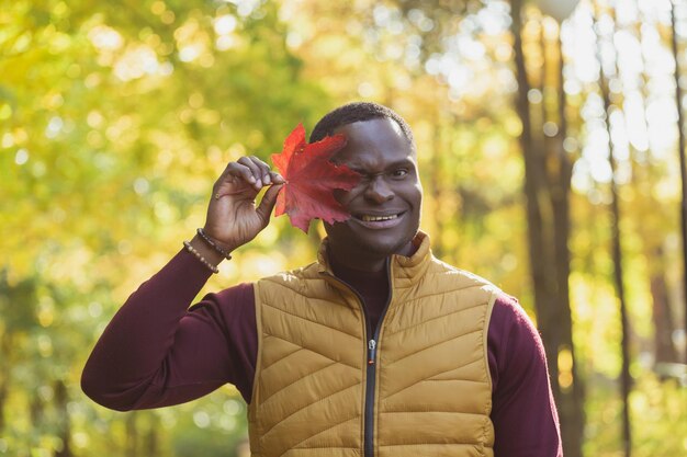 Portret afroamerykańskiego mężczyzny zakrywającego twarz jesiennym liściem klonu Jesienna natura Sezonowa jesienna moda