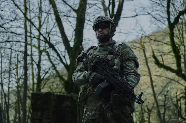 Zdjęcie portret airsoftowego gracza w profesjonalnym sprzęcie z karabinem maszynowym w lesie. żołnierz z bronią na wojnie