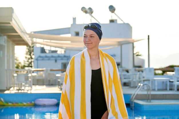 Portret Aktywnej Dziewczyny Nastolatka W Sportowym Stroju Kąpielowym, Kapeluszu Z Ręcznikiem Na Ramionach, Tło Odkryty Basen Pool