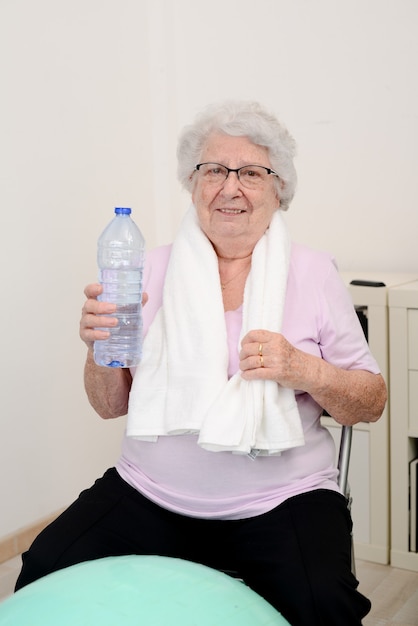 Zdjęcie portret aktywnej i dynamicznej starszej kobiety uprawiającej sport fitness w domu, trzymającej butelkę wody mineralnej