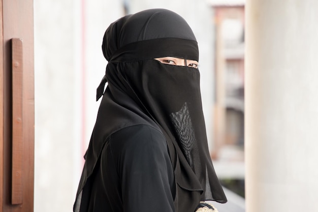 Zdjęcie portret arabskiej kobiety patrzącej na ciebie, zakrywającej twarz welonem z nikabu, tradycyjnej islamskiej maski na twarz, koncepcja dystansu społecznego w kulturze muzułmańskiej