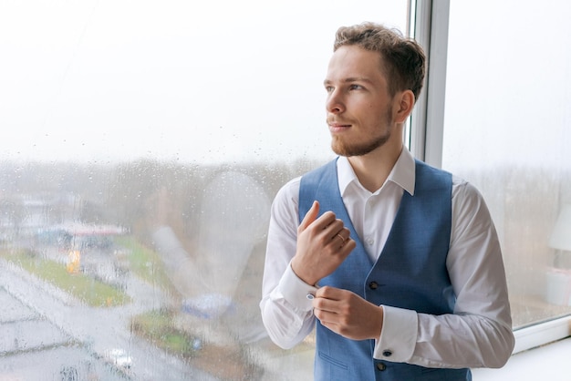 Portret aroganckiego, elegancko ubranego mężczyzny w niebieskim garniturze, korygującego guzika