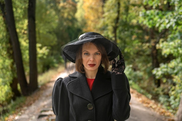 Portret arystokratycznej kobiety w czarnym kapeluszu z welonem jesienny park Kobieta w średnim wieku w vintage ubrania w stylu retro