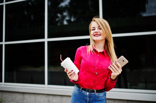 Portret atrakcyjna młoda kobieta pozuje z kawą i smartphone na zewnątrz centrum handlowego.