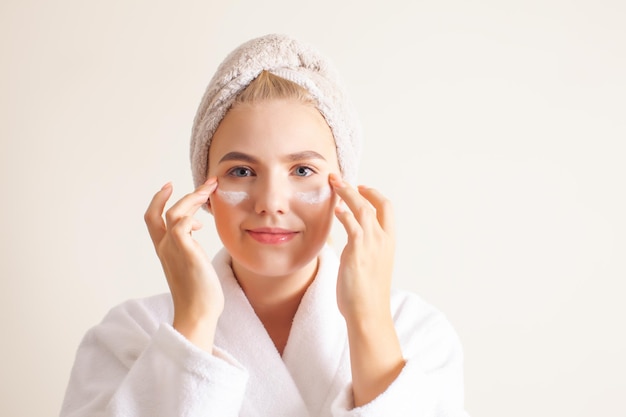 Portret atrakcyjna młoda kobieta z ręcznikiem na głowie co masaż twarzy kremem nawilżającym patrząc w kamerę Self procedury spa Naturalne piękno koncepcji