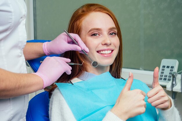 Portret atrakcyjna uśmiechnięta rudowłosa dziewczyna klienta imbir na fotelu dentystycznym w gabinecie dentystycznym. Nie jest strachem.