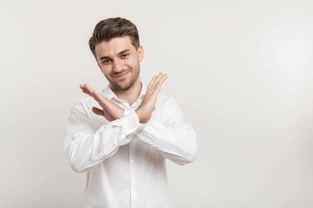 Portret atrakcyjnego uśmiechniętego faceta pokazującego znak stop skrzyżowane ręce na białym tle nad białym tłem
