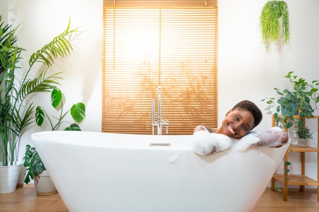 Portret atrakcyjnej afrykańskiej kobiety relaksującej się w wannie w przytulnej domowej łazience