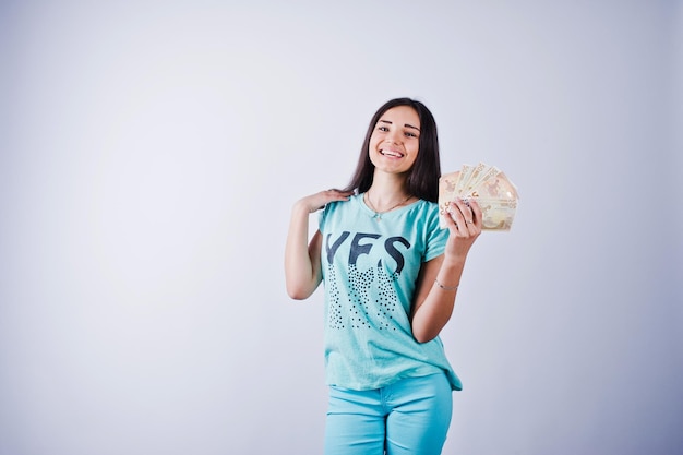 Portret atrakcyjnej dziewczyny w niebieskiej lub turkusowej koszulce i spodniach pozującej z dużą ilością pieniędzy w dłoni