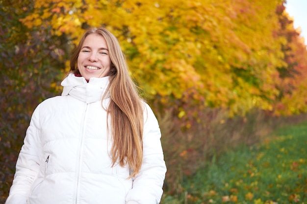 Portret atrakcyjnej, śmiejącej się pozytywnej kobiety z rudymi naturalnymi długimi włosami na sobie białą kurtkę