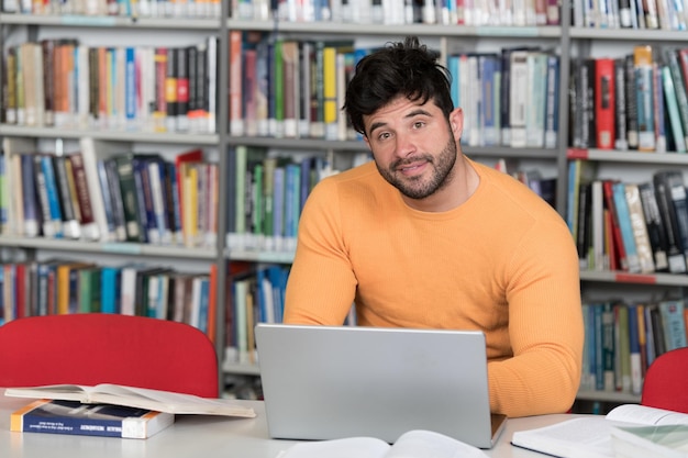 Portret atrakcyjnej uczennicy wykonującej jakąś pracę szkolną z laptopem w bibliotece
