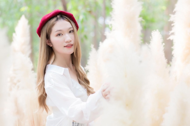 Portret Azjatycka piękna dziewczyna, która nosi białą sukienkę i czerwoną czapkę uśmiecha się w kolorowej suchej trawie