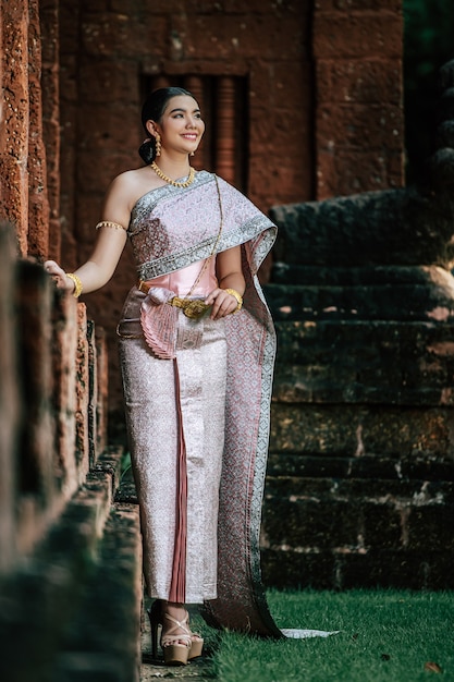 Portret Azjatycka urocza kobieta ubrana w piękną typową tajską kulturę tożsamości ubioru w Tajlandii w starożytnej świątyni lub słynnym miejscu z wdzięczną pozą
