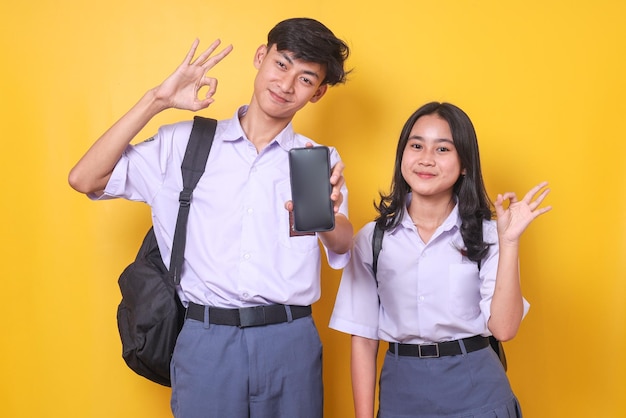 Portret azjatyckich studentów z torbami pokazującymi gest znaku ok podczas trzymania pustego makiety ekranu telefonu