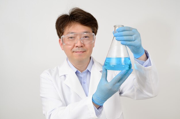 Portret azjatyckiego naukowca w średnim roku, ubrany w białą fartuch laboratoryjny i rękawiczki, trzymający w dłoni pojemnik doświadczalny.