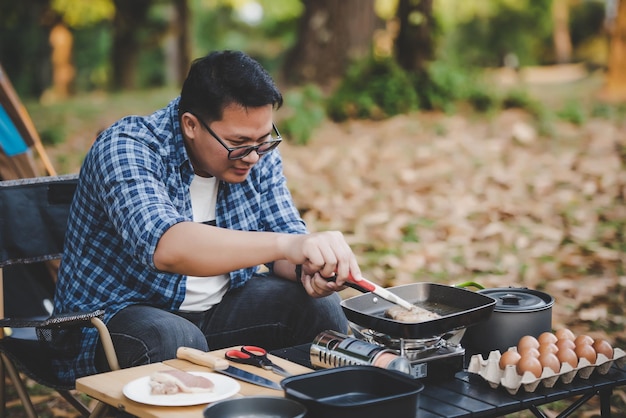 Portret Azjatyckiego Podróżnika Człowiek Okulary Stek Wieprzowy Smażenia Bbq W Patelni Patelni Lub Garnka Na Kempingu Gotowanie Na świeżym Powietrzu, Podróżowanie, Koncepcja Stylu życia Na Kempingu