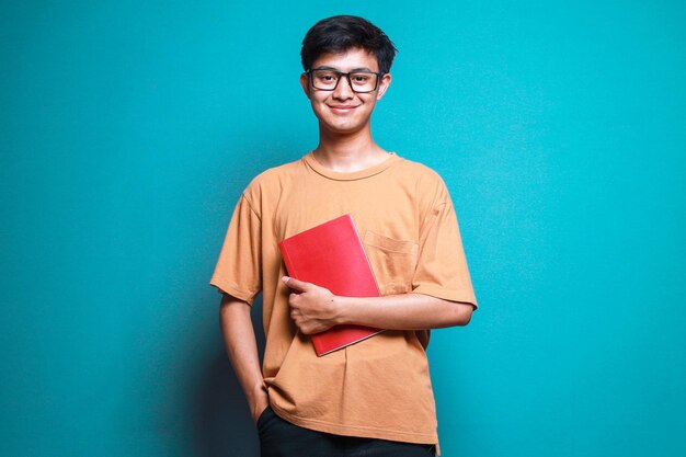 Portret azjatyckiego studenta noszącego okulary i trzymającego książki na błękitnym tle