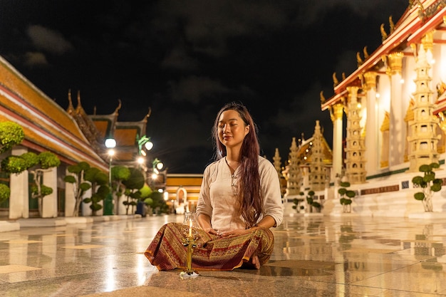 Portret azjatyckiej buddyjskiej kobiety w tradycyjnym stroju Tajlandii, siedzącej do medytacji, aby oddać szacunek posągowi Buddy w Wat Suthat Thepwararam w buddyjski święty dzień Buddyjski dzień sabatu
