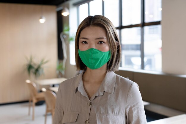 Zdjęcie portret azjatyckiej kobiety noszącej maskę w kreatywnym biurze. dystans społeczny w miejscu pracy biura biznesowego podczas pandemii koronaawirusa covid 19.