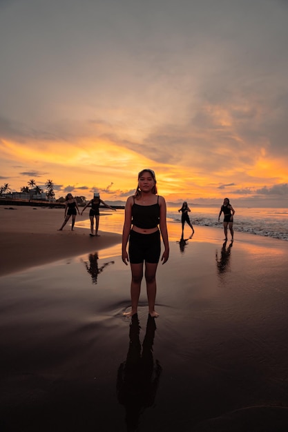 Portret azjatyckiej kobiety w czarnych ubraniach stojącej na plaży z przyjaciółmi tańczącymi za nią