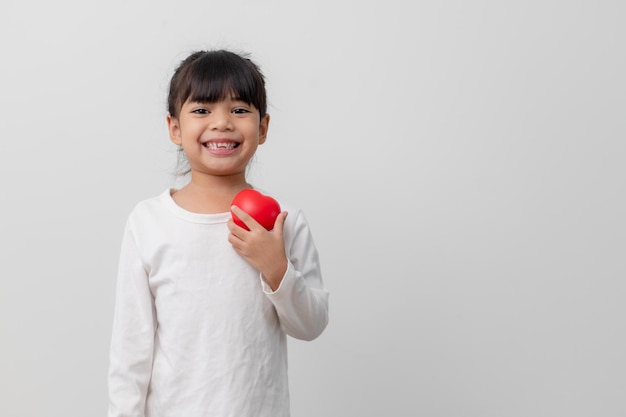 Portret azjatyckiej małej dziewczynki dziecka trzymającego czerwony znak serca na białym tle