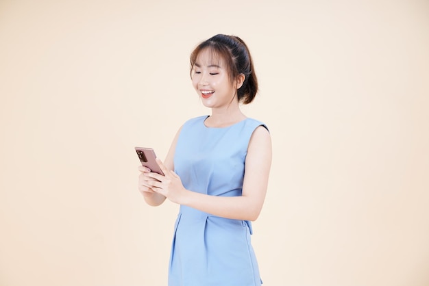 Portret azjatyckiej młodej pięknej i wesołej kobiety korzystającej z inteligentnego telefonu na białym tle