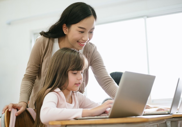 Portret azjatyckiej nauczycielki pomagającej uczennicy używa laptopa w klasie komputerowej Edukacja Koncepcja nauki i technologii w szkole podstawowej