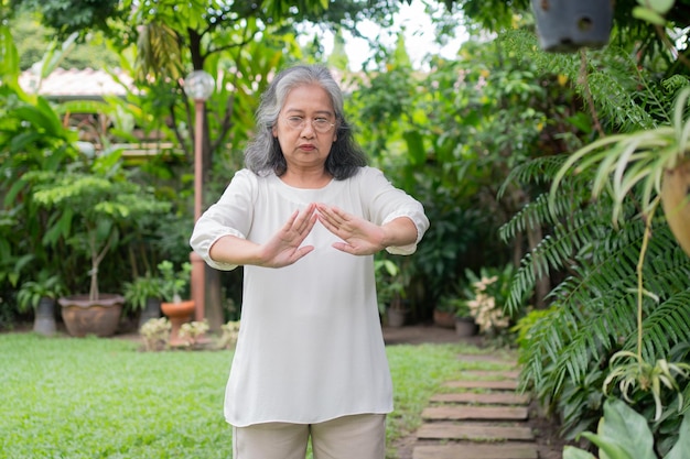 Portret azjatyckiej starszej kobiety wykonującej ćwiczenia jogi i rozciągające w ogrodzie podczas treningu