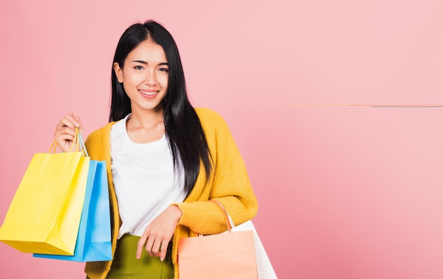Portret azjatyckiej szczęśliwej pięknej młodej kobiety nastolatka kupująca uśmiechnięta stojąca podekscytowana trzymająca torby na zakupy online kolorowe wielokolorowe latem, studio strzał odizolowane na różowym tle z miejsca kopiowania
