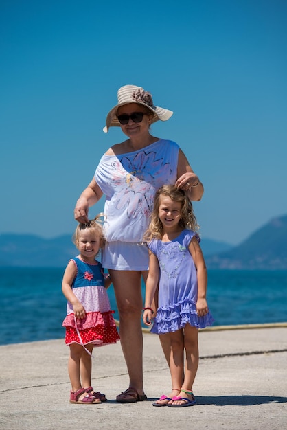 Portret babci z jej uroczymi małymi wnuczkami trzymającymi się za ręce, stojąc na wybrzeżu podczas letnich wakacji