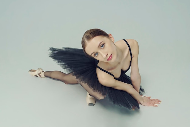 Portret baletnicy w czarnej tutu leżącej na podłodze, opierając się na dłoniach widok z góry