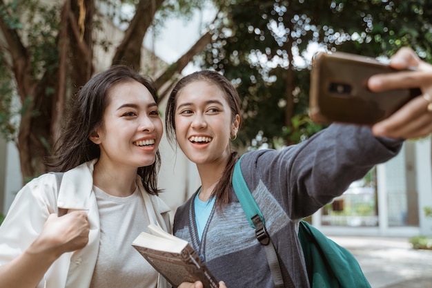 Portret bardzo szczęśliwych i uśmiechniętych studentów robi sobie selfie na podwórku kampusu