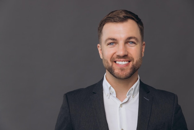 Portret białego tysiącletniego biznesmena izolowanego na szarym tle w studiu pozującego zadowolonego, udanego mężczyzny w formalnym garniturze, szczęśliwego i uśmiechniętego zębami