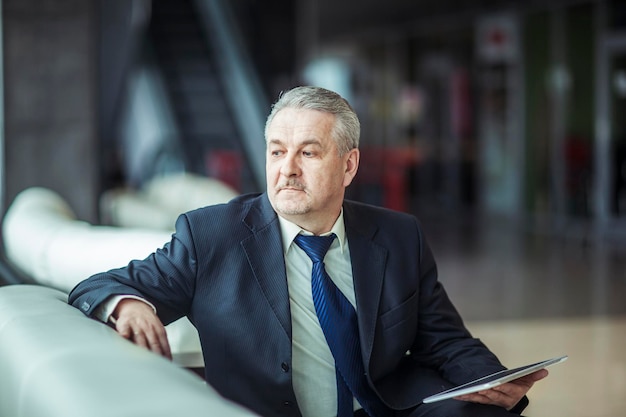 Portret biznesmena z cyfrowym tabletem siedzącym na krześle przed biurem