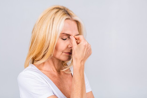 Zdjęcie portret blond podkreślił zmęczoną, zmęczoną, dojrzałą starszą kobietę na białym tle na szarym tle koloru białego.