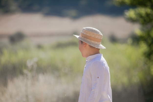 Portret blond włosianego chłopca w słomkowym kapeluszu z niewyraźnym letnim tłem zieleni