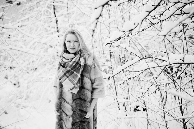 Portret blondynka w okularach, czerwonym futrze i szaliku w zimowy dzień.