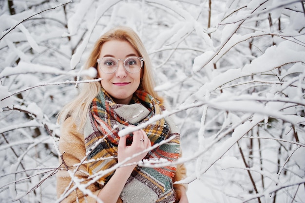 Portret blondynka w okularach, czerwonym futrze i szaliku w zimowy dzień.