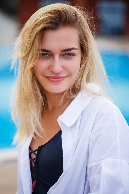 Portret blondynki w białej koszuli siedzi przy basenie i patrzy w kamerę