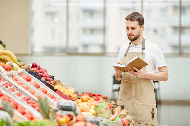 Portret Brodatego Mężczyzny W Fartuchu Stojącego Przy Stoisku Z Owocami I Warzywami Na Rynku Rolników Podczas Sprzedaży świeżych Produktów