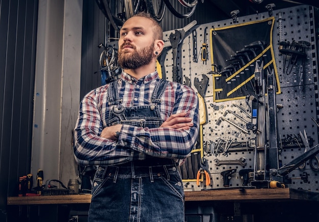 Portret Brodaty mechanik rowerowy ze skrzyżowanymi rękami na tle stoiska narzędziowego.