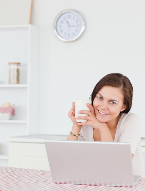 Portret brunetka używa jej laptop i mieć herbaty