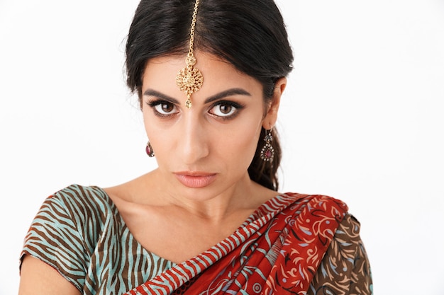 Portret brunetki hindus dziewczyna ubrana w tradycyjny strój indyjski lehenga choli lub saree sukienkę i biżuterię etniczną na białym tle nad białą ścianą